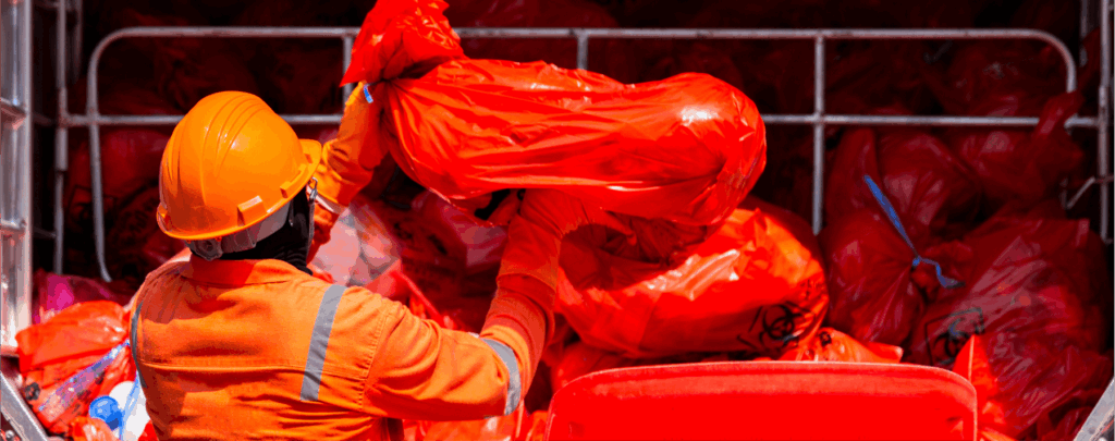 Worker handling red biohazard waste bags.