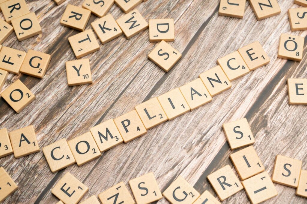 Scrabble tiles spell 'compliance' on wooden background.