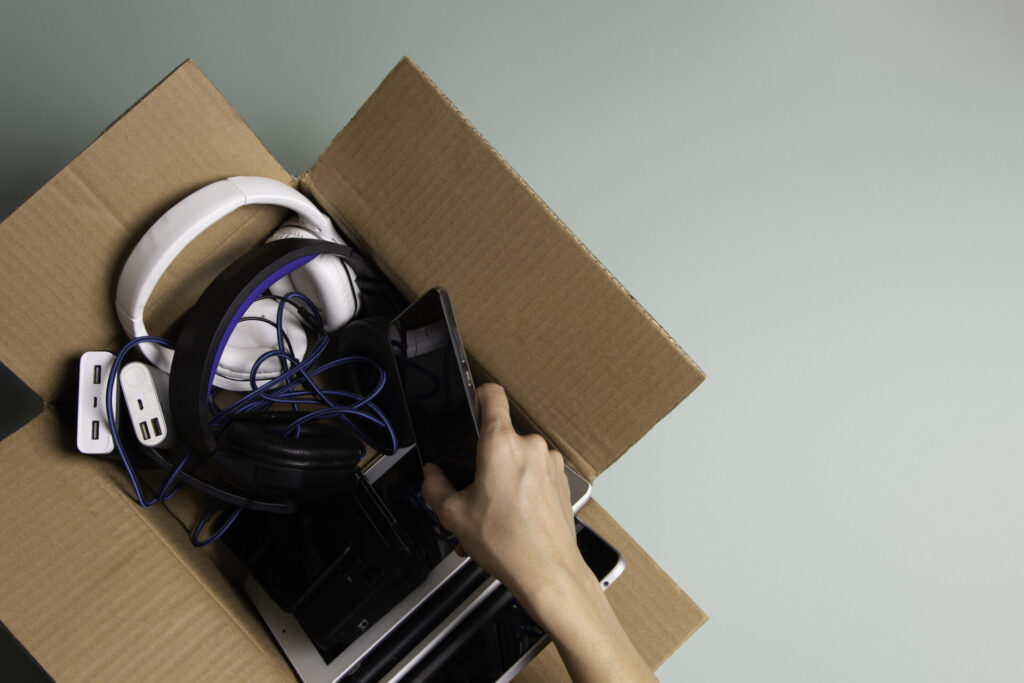 Woman hand collect old used computers, digital tablets, smartphones, electronic devices to cardboard box. Top view. Donation, charity, e-waste, electronic gadgets for reuse, refurbish, recycle concept.